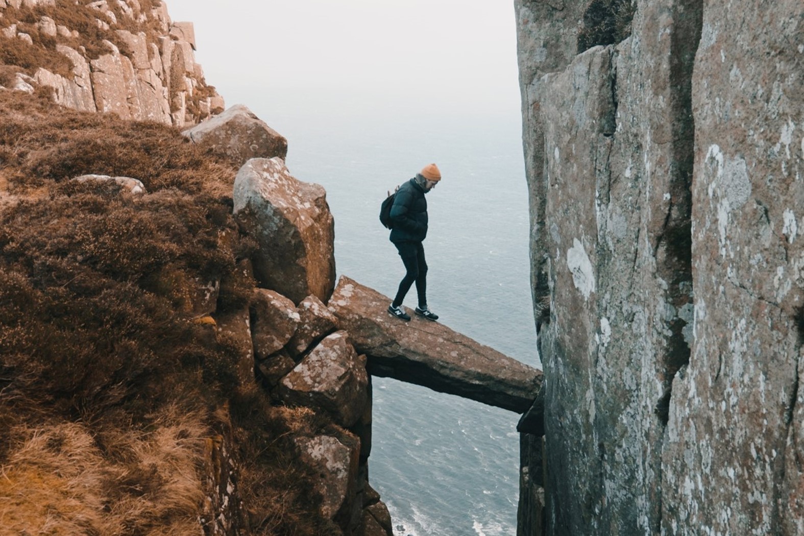 Homme prenant des risques sur un pont en bloc de pierre en équilibre au dessus d’un précipice.